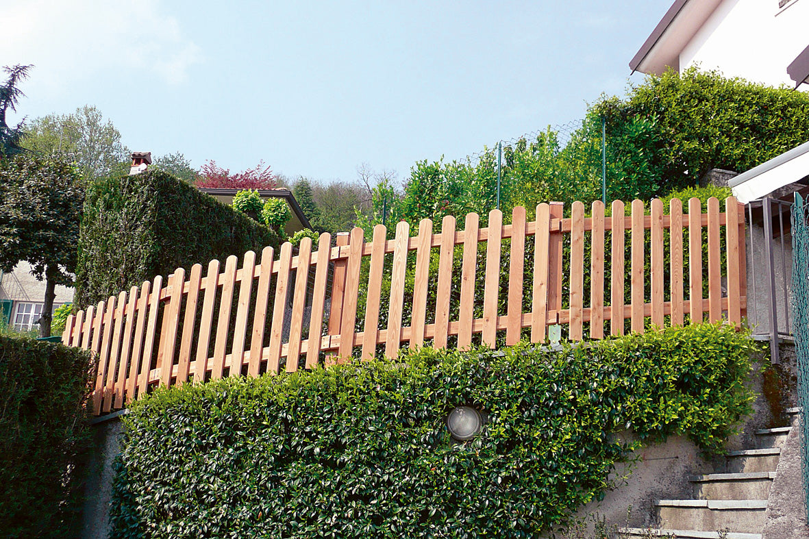 Recinzione in legno e siepe verde in un giardino curato.