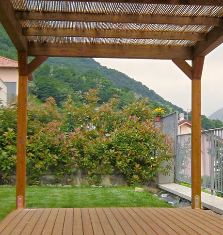 Vista da un pergolato in legno su un patio con giardino e colline verdi sullo sfondo.