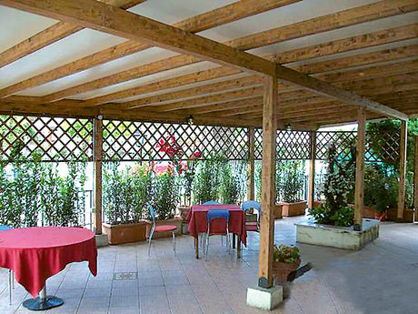Patio esterno con tavoli coperti da tovaglie rosse e strutture in legno.